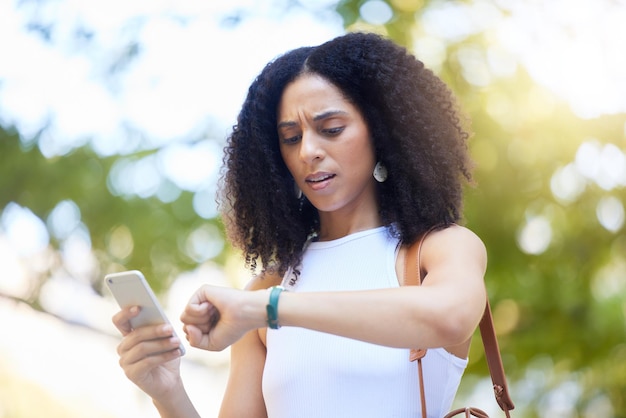 Black woman phone and checking time on watch for schedule appointment or planning in the park African American female monitoring smart watch for busy day in the outdoors with smartphone in nature