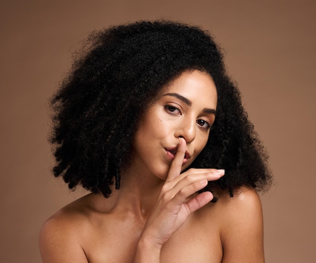 사진 스튜디오 배경에서 스킨케어 화장품과 신체 건강에 대한 비밀을 위해 입술에 손가락을 대고 있는 흑인 여성 초상화
