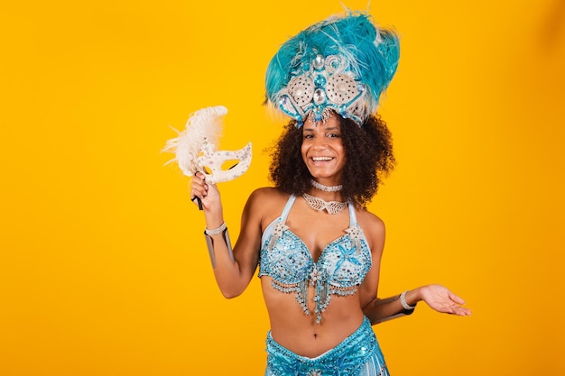 Black woman queen of brazilian samba school with blue carnival clothes and crown of feathers holding mask welcome