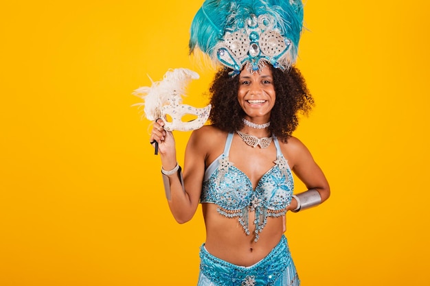 Black woman queen of Brazilian samba school with blue carnival clothes and crown of feathers holding mask
