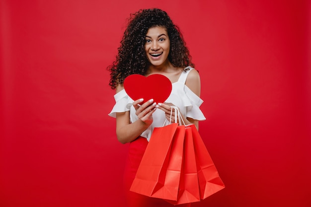Чернокожая женщина читает от сердечной формы валентинка и хозяйственные сумки на красной стене