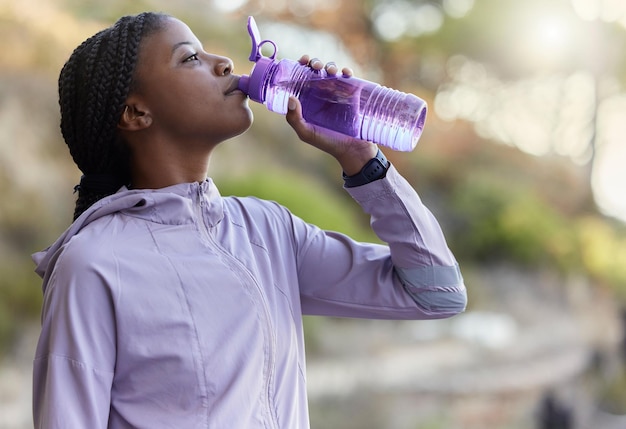 Black woman runner drinking water bottle or rest for hydration wellness and health in summer training Woman running and drink water for exercise workout or fitness at nature park in California