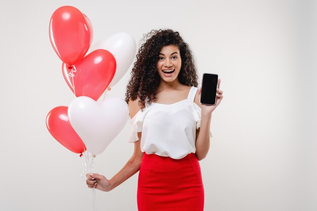 Black woman showing copy space blank phone screen with heart shaped balloons isolated