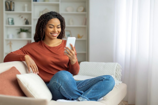 Black woman sitting on couch using cell phone