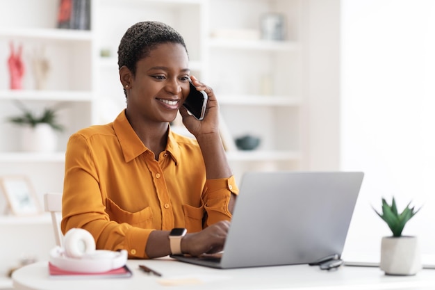 전화 통화를 하는 노트북과 함께 테이블에 앉아있는 흑인 여성