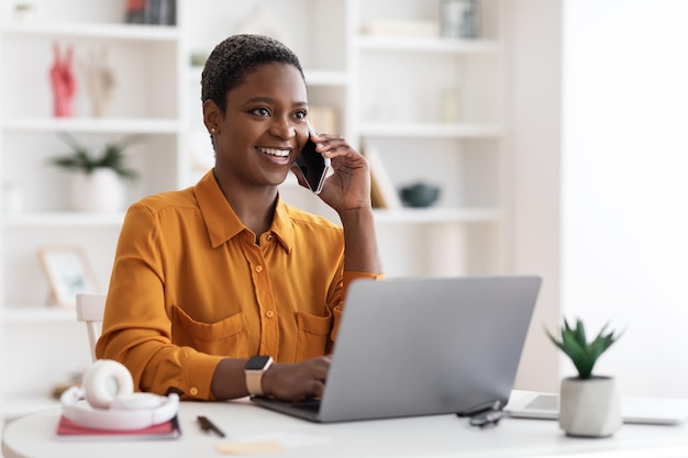 Black woman sitting at table with laptop having phone conversation