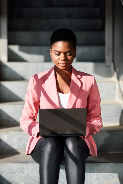 Black woman sitting on urban steps working with a laptop computer.