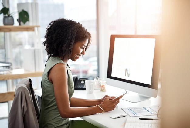 Black woman smartphone and office smile at desk for social media communication and typing text Female business person at computer screen contact and notification with meme internet and app