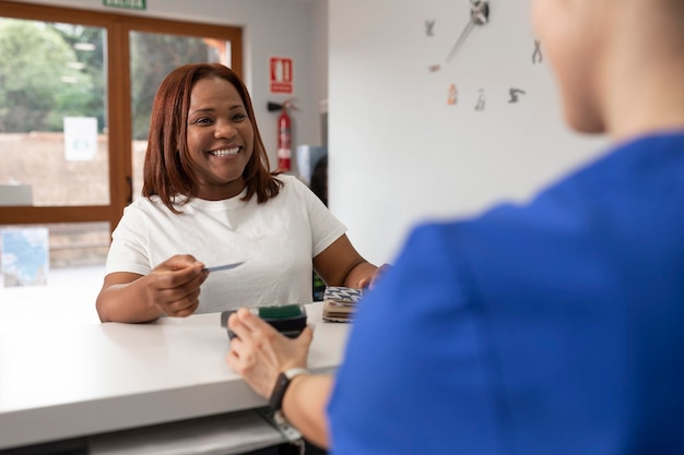 黒人女性が、歯科医院で受けた良いサービスの見返りとして支払う前に、クレジット カードを持って喜んで微笑んでいる