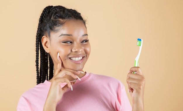 La donna di colore sorride con denti bianchi e perfetti mentre tiene in mano uno spazzolino da denti