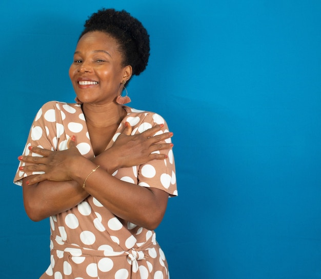 Black woman smiling and  hugging herself  with  a blue wall