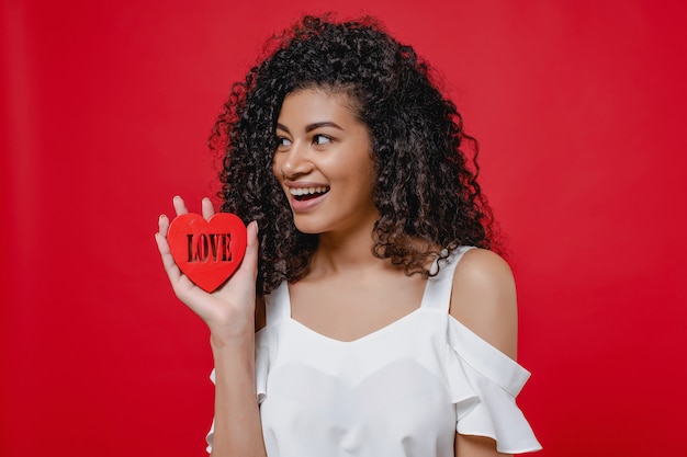 Black woman smiling with heart shape figure with love letters on red wall