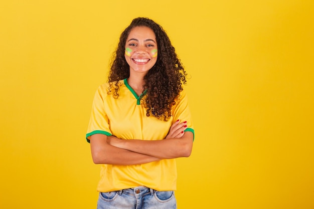 чернокожая женщина, футбольная фанатка из Бразилии, скрестив руки, уверенная в себе и улыбающаяся