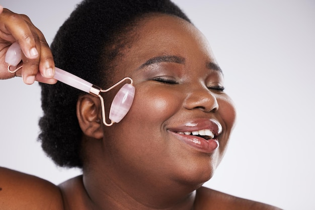 Black woman studio and skincare rose quartz roller for cosmetic beauty smooth and healthy glow on face Model happy and massage skin for health wellness and beauty by gray background with smile