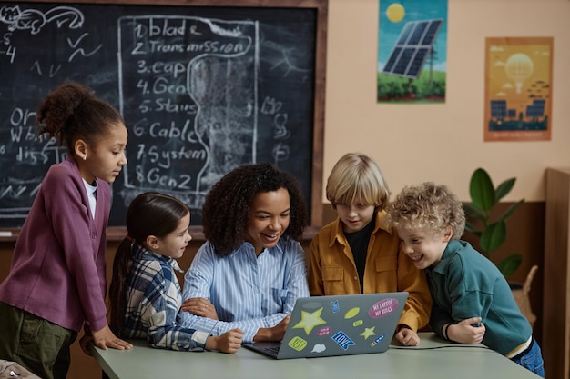 Foto insegnante nera che usa il portatile con bambini scolastici felici che guardano