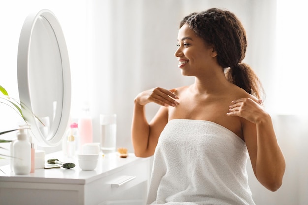 Photo black woman touching her flawless skin while looking in mirror at home