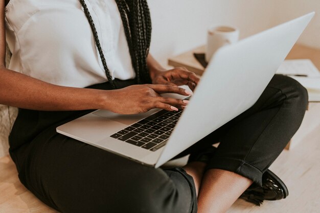 Black woman using a notebook on her laps on a wooden floor