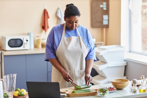 Donna di colore che indossa un grembiule in cucina e segue un video di  cucina online