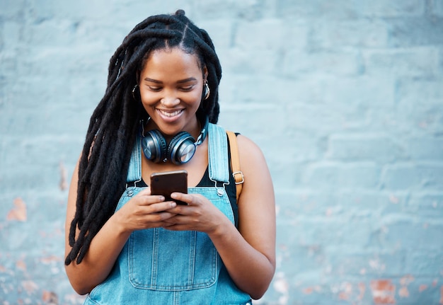 デジタルチャットアプリを入力するソーシャルメディア用の5gスマートフォンを持つ黒人女性、または青い壁の背景スペースのモックアップで場所を確認する若者のオンラインウェブサイトネットワーキングのための携帯電話でティーンエイジャーのz世代の女の子