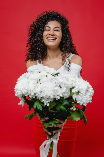 Black woman with bouquet of white flowers wearing skirt isolated on red