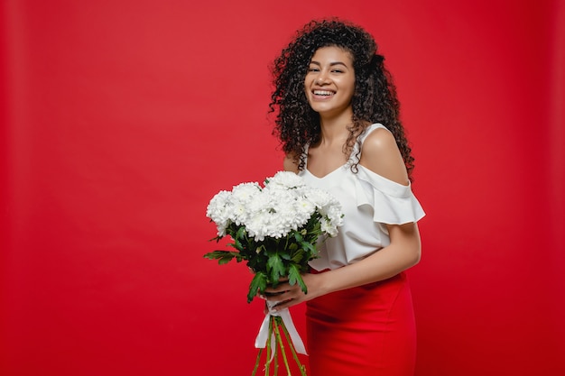 Black woman with bouquet of white flowers wearing skirt isolated on red