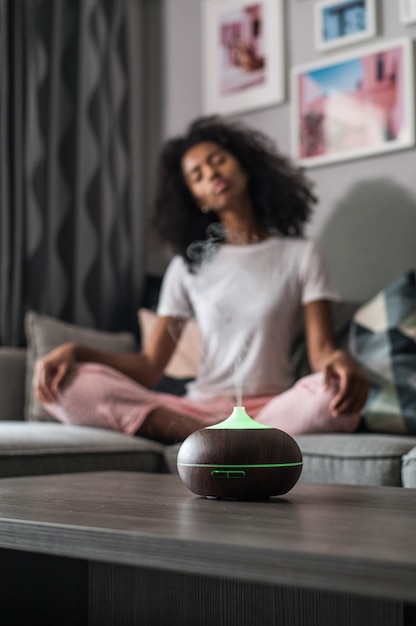 Black woman with curly hair sitting on sofa in Lotus pose and meditating