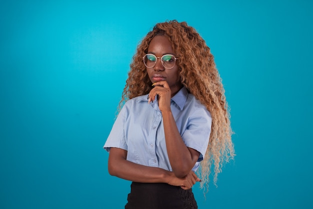 Black woman with curly hair in studio photo wearing blue shirt and black skirt and making various facial expressions.