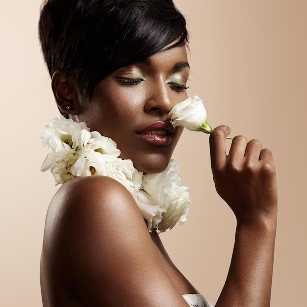 Black woman with ideal skin and closed eyes sniffing a flower