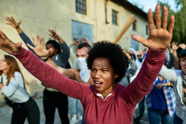 Black woman with raised arms shouting while participating in public demonstrations on the streets