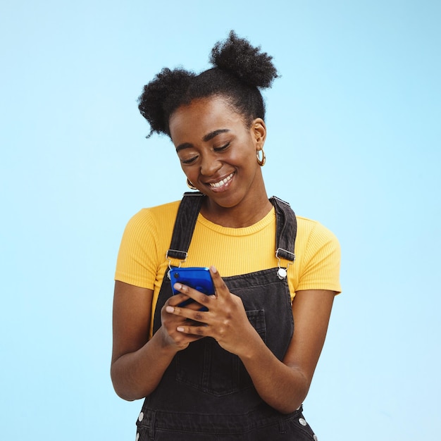 Black woman with smartphone in hands smile and happy with chat or social media communication isolated on blue background technology happiness and gen z youth phone with internet wifi and mockup