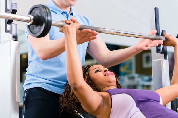 Black woman with Trainer lifting weights in gym for fitness