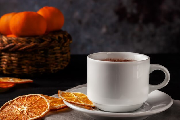 黒い木製の背景に、乾燥したオレンジスライスとお茶のカップ