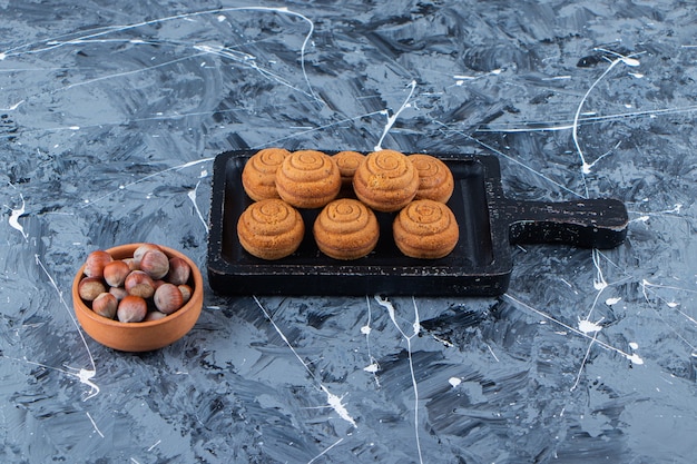 A black wooden board of sweet fresh round cookies for tea with healthy nuts on a marble surface .