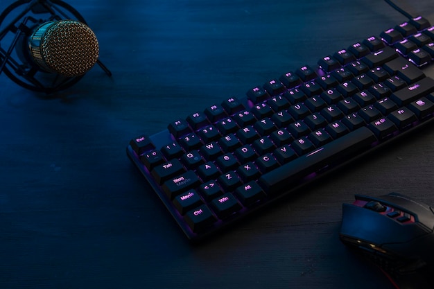 Black wooden desk with a gamer keyboard mouse and microphone to broadcast while playing online