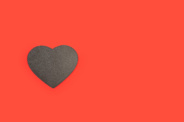 A black wooden heart with copy space on a red background