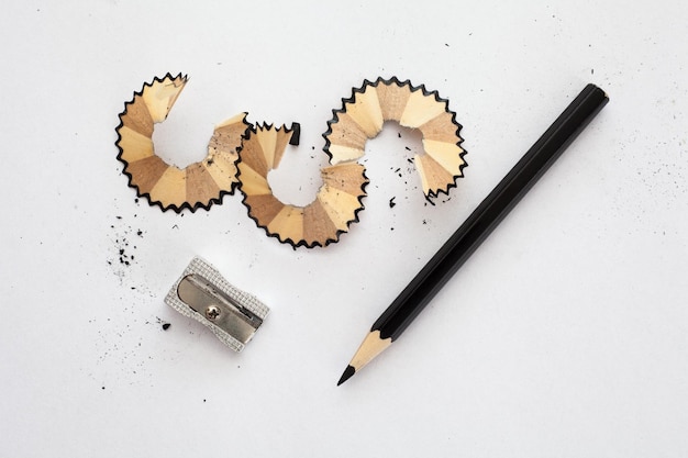 Фото Черная деревянная острица для карандашей и осколки карандаша на белой бумаге