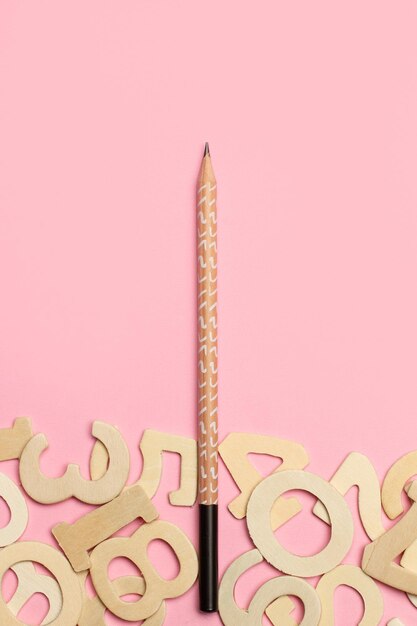 A black wooden pencil and wooden numbers on a pink background with copy space