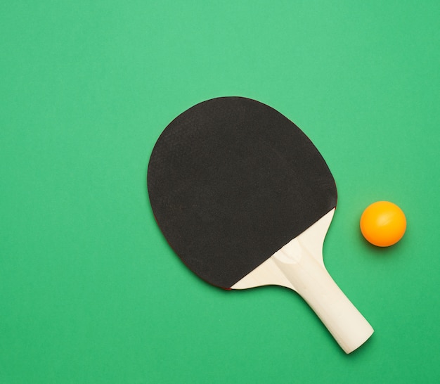 Black wooden racket and plastic orange table tennis ball, top view