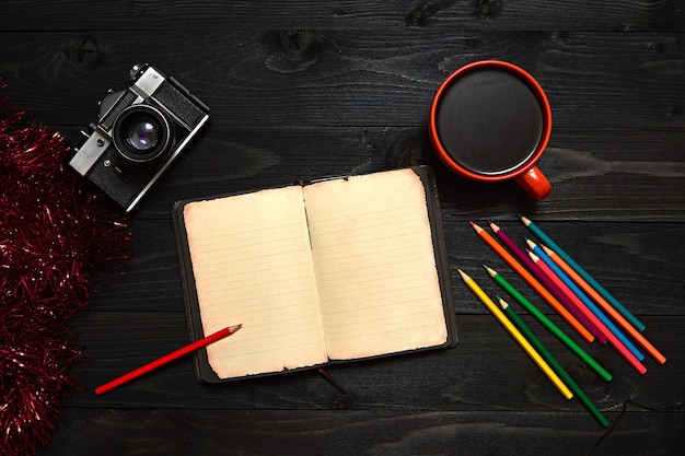 a black wooden table with colored pencils, a notebook, a camera and an orange coffee mug