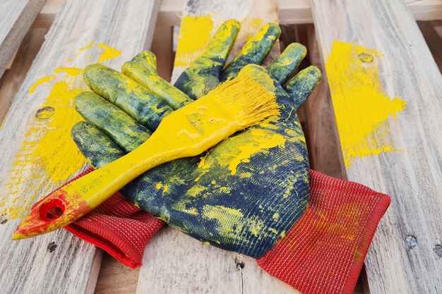 Black work protective gloves and paint brush smeared with yellow painted lies on a wooden pallet