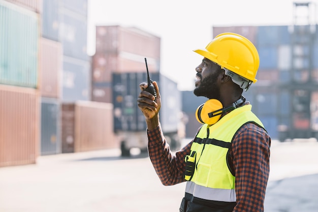 Black worker african working engineer foreman radio control in\
port cargo shipping customs container yard