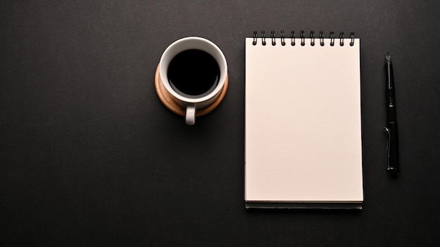 Black workspace background with coffee empty spiral notepad and copy space