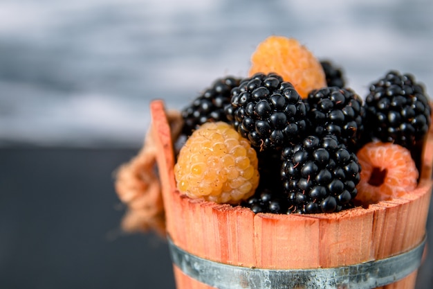 Black and yellow raspberries in a wooden basket on grey wooden background. 