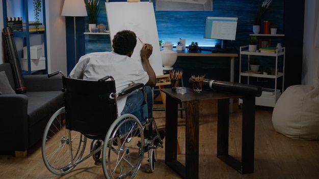 Black young artist with handicap drawing vase on canvas