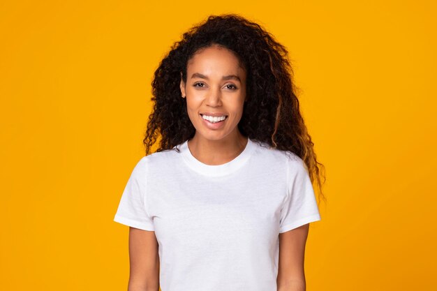 Black young lady with curly hair expressing positivity yellow background