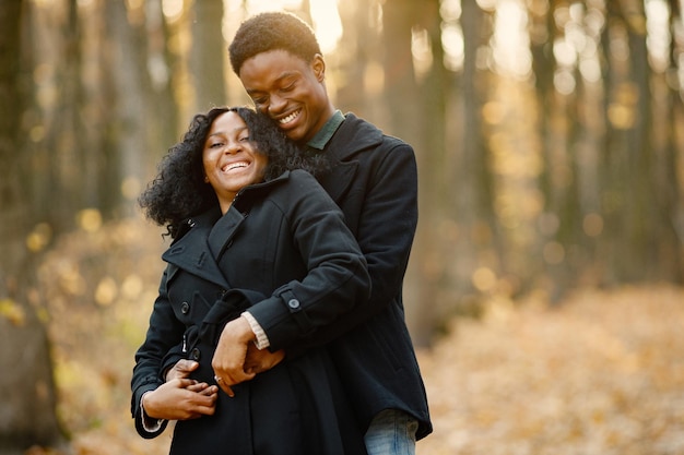 black young man and his girlfriend hugging. romantic couple walking in autumn park. man and woman wearing black coats.