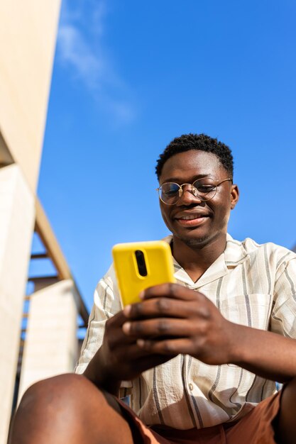 Black young man sitting on stairs outdoors using mobile phone Vertical image Copy space