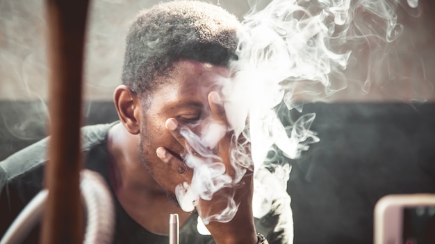 black young man smoking while touching his face with her hand