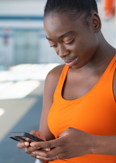 Black young woman using her smartphone sitting in a bench at the heated swimming pool