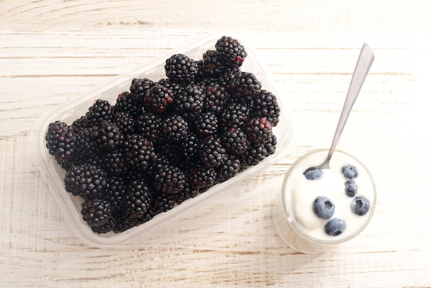 Blackberries in a container, a glass of yogurt and blueberries,  